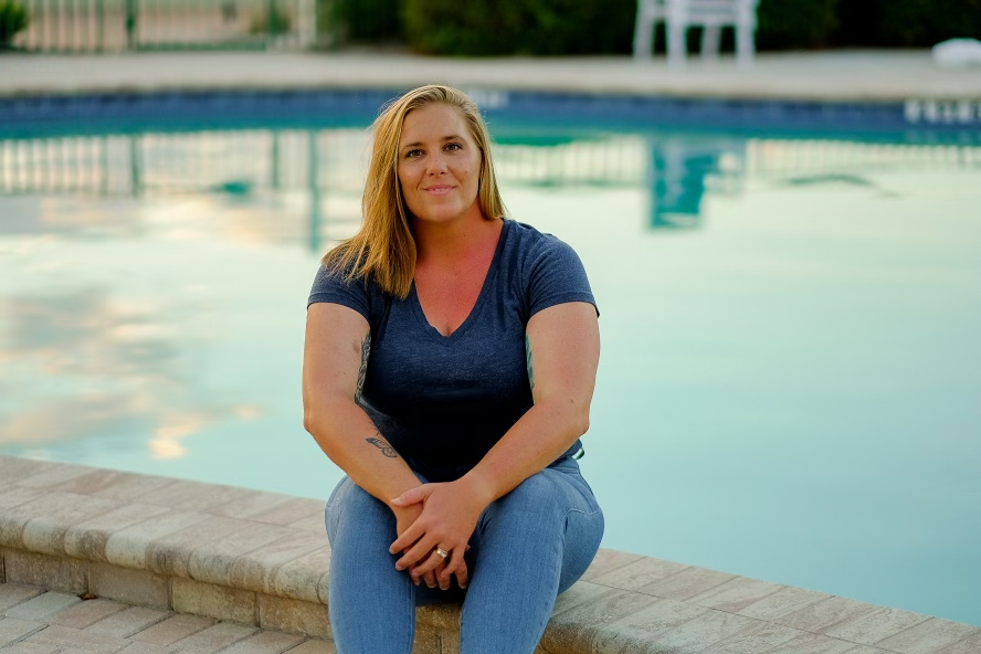 Amanda, a swim instructor, sitting by the edge of a swimming pool, smiling warmly and looking approachable and friendly